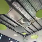 Circular acoustic ceiling panels with integrated downlights providing both sound absorption and ambient illumination.